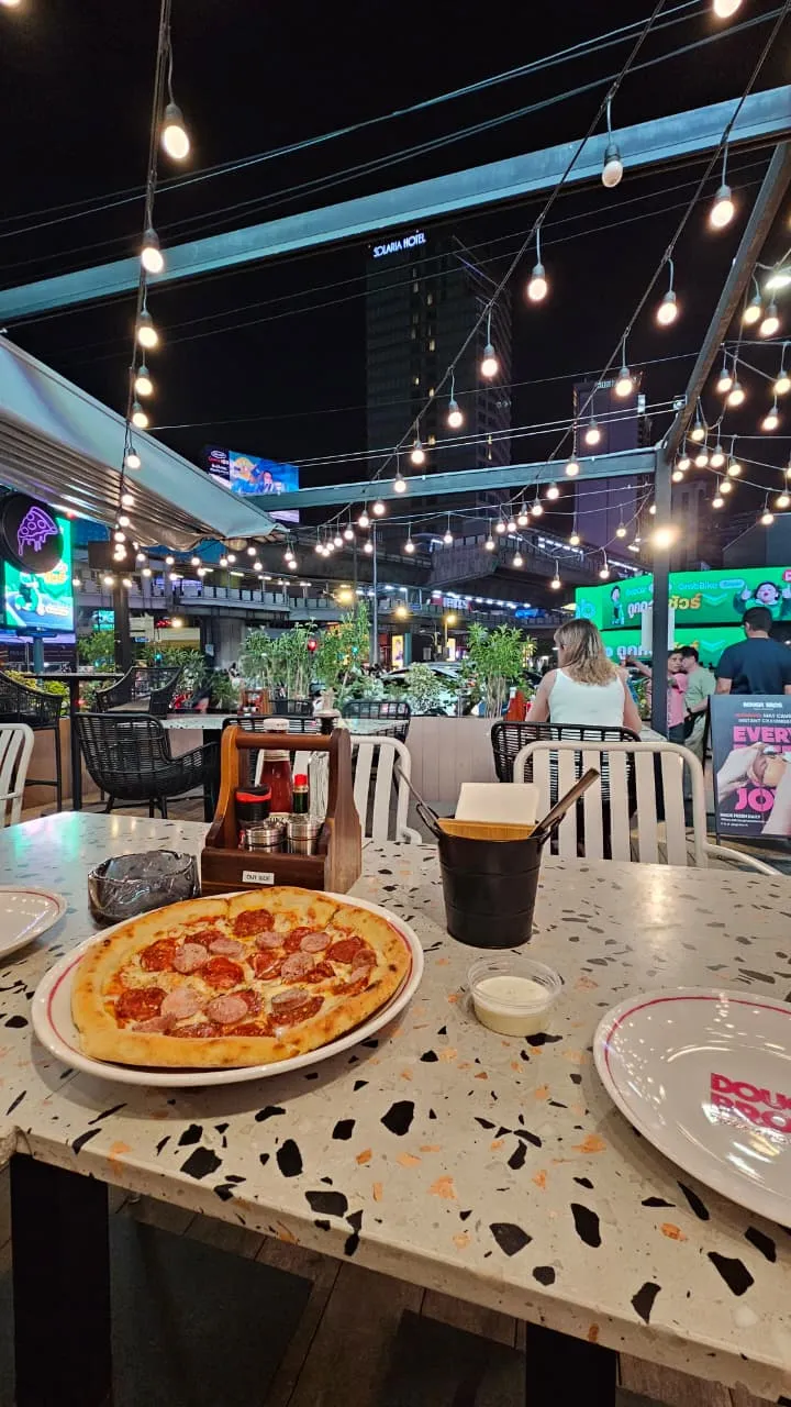Pizza on an outdoor restaurant table beneath strings of lights at night.